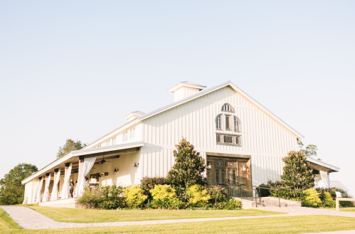 A charming white barn with large doors and greenery, set against a clear blue sky.
