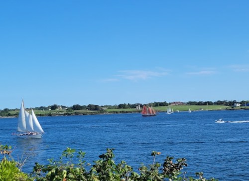 Sailboats and a motorboat on a calm blue sea under a clear sky, with green hills in the background.