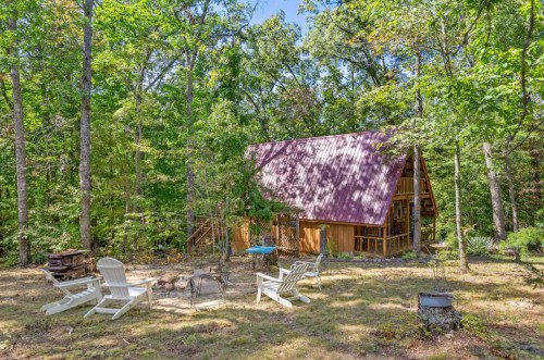 A cozy cabin with a purple roof surrounded by trees, featuring outdoor seating and a fire pit.