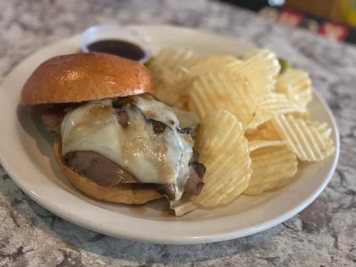 A plate with a cheeseburger topped with mushrooms and a side of ridged potato chips, accompanied by a dipping sauce.