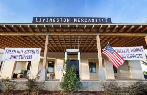 Exterior of Livingston Mercantile with signs for fresh biscuits, coffee, and supplies, featuring an American flag.