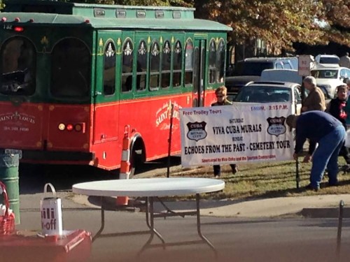 A red trolley bus parked near a banner for a cemetery tour titled "Viva Cuba Murals: Echoes from the Past."