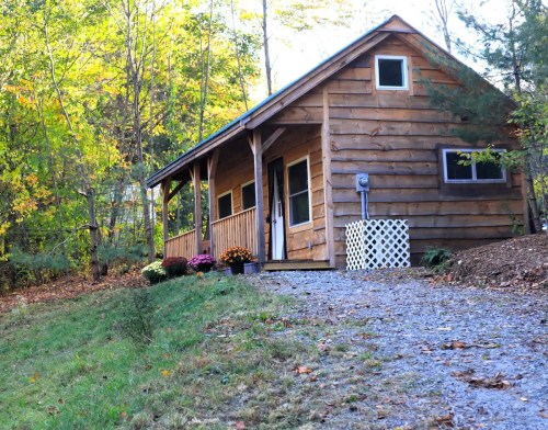 A cozy wooden cabin surrounded by trees and colorful autumn foliage, with a gravel path leading up to it.