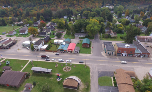 Aerial view of a small town with colorful trees, houses, and a main street lined with shops and vehicles.