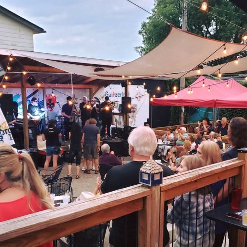 A lively outdoor music event with a crowd enjoying performances under string lights and tents.