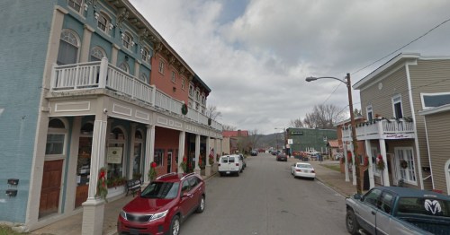 A quaint street scene featuring colorful buildings, parked cars, and holiday decorations in a small town.