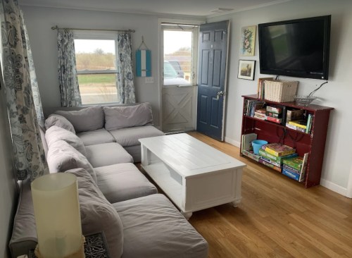 Cozy living room with a gray sectional sofa, white coffee table, and a bookshelf filled with games and books.
