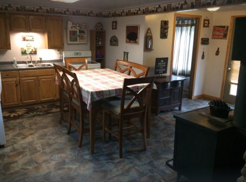 Cozy kitchen with wooden cabinets, a large table, and a vintage decor, featuring a stove and a door leading outside.