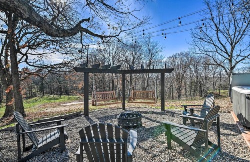 A cozy outdoor seating area with wooden swings, chairs, and a fire pit, surrounded by trees and string lights.