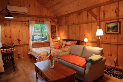 Cozy wooden cabin interior featuring a bed, sofa, table, and large window with natural light.