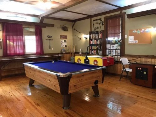 A cozy game room featuring a blue pool table, wooden floors, and various decorations on the walls.