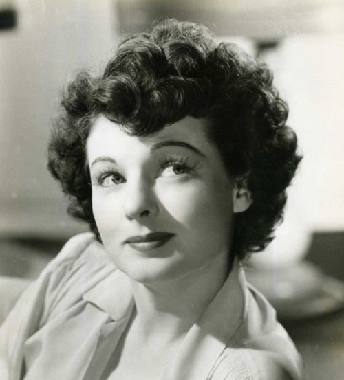 Black and white portrait of a woman with curly hair, looking thoughtfully to the side.