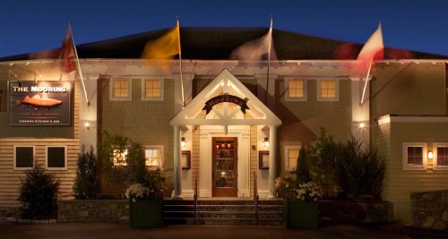 The exterior of a seafood restaurant at night, featuring flags and a welcoming entrance with warm lighting.