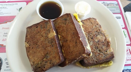 Three slices of French toast with a side of syrup and a dollop of butter on a white plate.