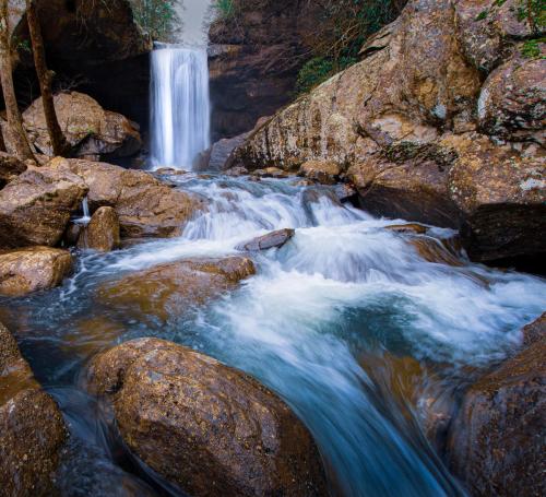 A serene waterfall cascades over rocks, surrounded by lush greenery and flowing water in a tranquil natural setting.