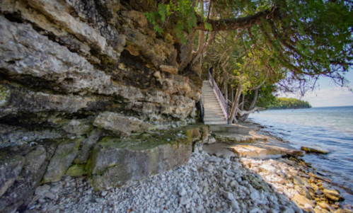 A rocky shoreline with steps leading up to a wooded area beside calm water.
