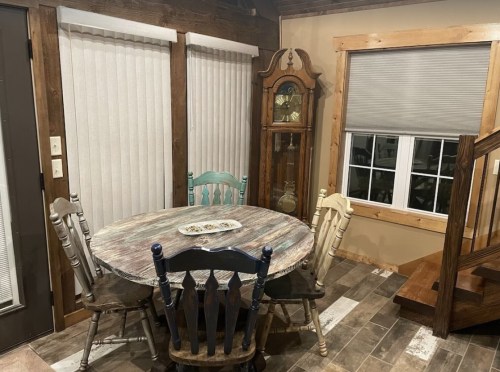 A cozy dining area with a round table, four chairs, a grandfather clock, and wooden accents in a rustic setting.