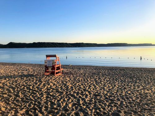 A lifeguard stand on a sandy beach with calm water and a clear sky at sunrise.