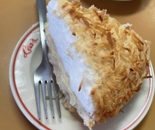A slice of coconut cream pie on a plate with a fork, featuring a toasted coconut topping and fluffy meringue.