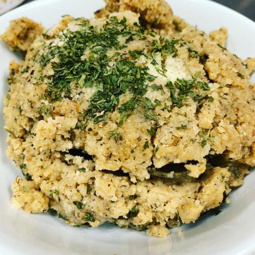 A close-up of a bowl filled with a textured, herb-seasoned dish, likely a stuffing or bread mixture.