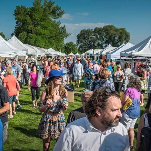 A bustling outdoor market with people browsing tents and stalls under a clear blue sky.