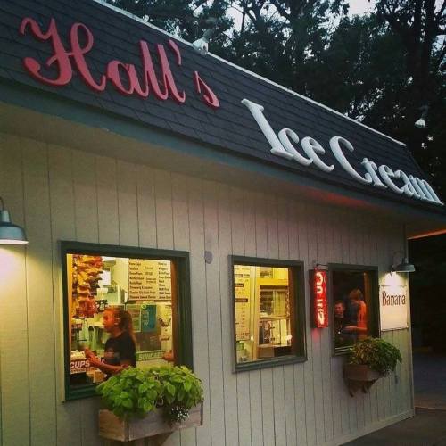 A cozy ice cream shop with a sign reading "Hall's Ice Cream," featuring two windows and a banana-themed decoration.
