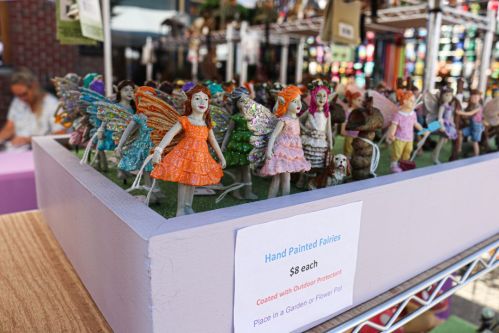 A display of colorful hand-painted fairy figurines for sale, set in a garden or flower pot.