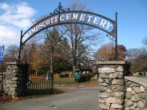 Archway sign reading "Swampscott Cemetery" with stone pillars and trees in the background on a clear day.