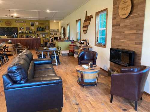 Cozy café interior with leather seating, wooden floors, and a fireplace, featuring a bar and shelves of drinks.