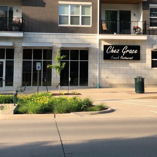 Exterior view of "Chez Grace," a French restaurant, featuring a sign and landscaped area in front.
