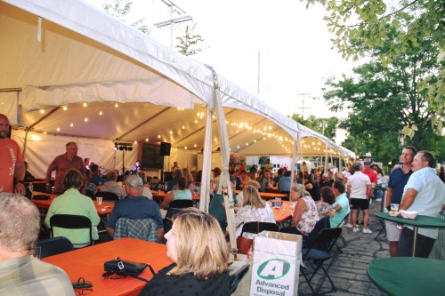 A lively outdoor event under a tent, with people seated at tables enjoying music and socializing.