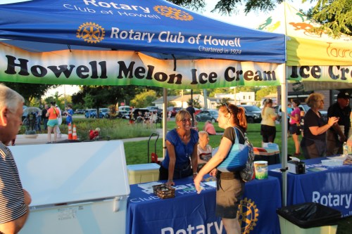 A woman at a booth for Howell Melon Ice Cream, with people enjoying the event in the background.