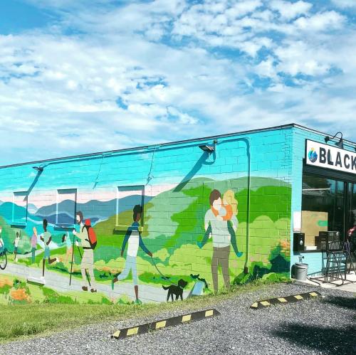 Colorful mural on a building depicting people walking dogs and enjoying nature against a scenic landscape.