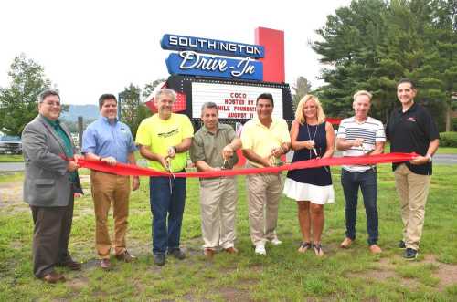 A group of people holding scissors cut a red ribbon in front of the Southington Drive-In sign during a ceremony.