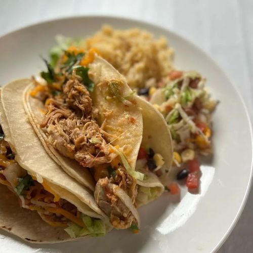 Three tacos filled with shredded chicken, cheese, and lettuce, served with rice and a side of salad.