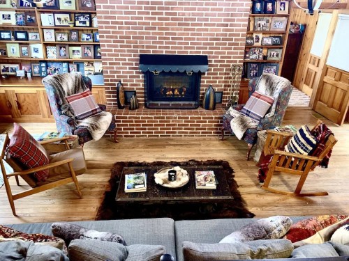 Cozy living room with a brick fireplace, two armchairs, a wooden coffee table, and shelves filled with family photos.
