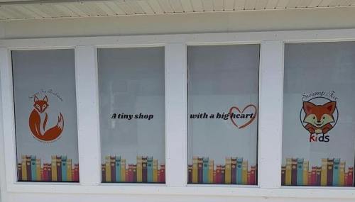 Windows of a shop featuring a fox logo, colorful books, and text: "A tiny shop with a big heart" and "Swamp Fox for Kids."