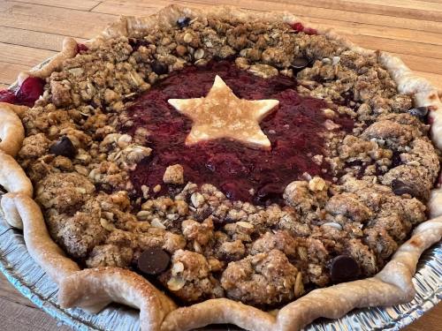 A homemade pie with a crumbly topping, filled with red fruit and topped with a star-shaped pastry in the center.