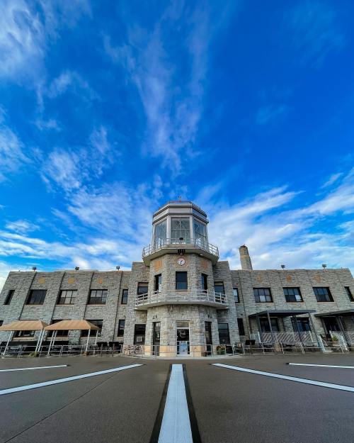 Historic stone building with a tower, clock, and large windows, set against a blue sky with scattered clouds.