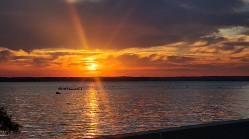 A vibrant sunset over a calm lake, with golden rays reflecting on the water and clouds in the sky.