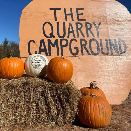 A display of pumpkins in front of a sign that reads "The Quarry Campground" against a clear blue sky.