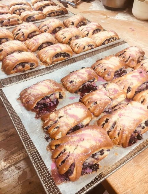 Freshly baked pastries filled with blueberries, arranged on cooling racks in a rustic kitchen setting.
