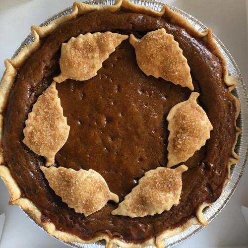 A pumpkin pie with a golden crust, topped with decorative leaf-shaped pastries around the edge.