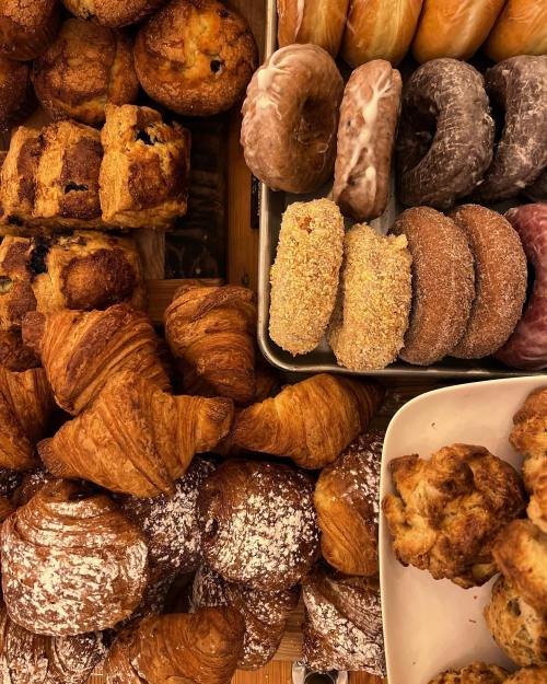 A variety of baked goods including croissants, muffins, and donuts arranged on trays.