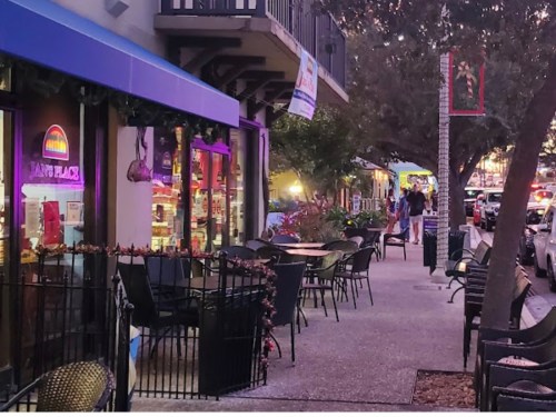 A vibrant street scene with outdoor seating, shops, and people walking in the evening light.