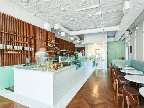 A modern café interior featuring a glass display case with baked goods, wooden shelves, and stylish seating.