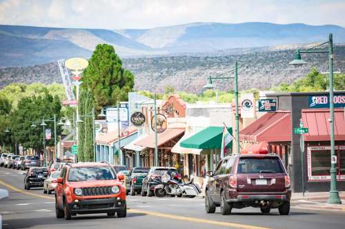 A busy street lined with colorful shops and vehicles, set against a backdrop of mountains and blue skies.