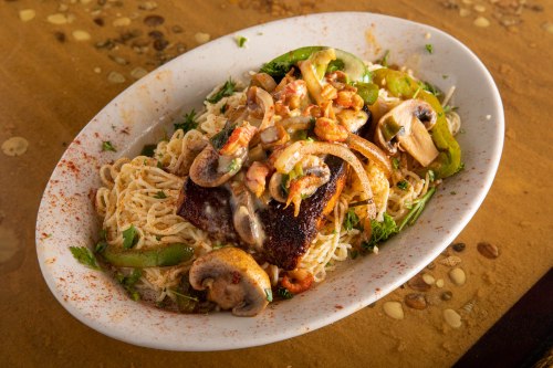 A plate of pasta topped with sautéed mushrooms, onions, green peppers, and a piece of grilled fish.