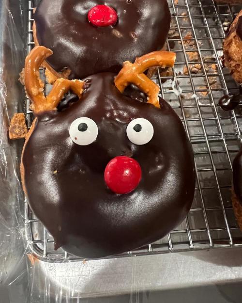 A chocolate donut decorated as a reindeer with pretzel antlers, candy eyes, and a red candy nose.
