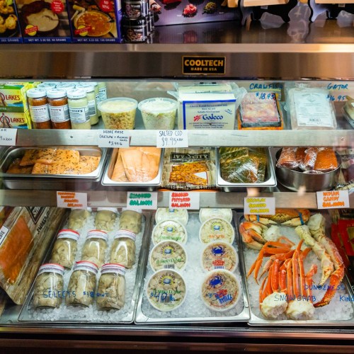 A display case filled with various seafood items, including crab, shrimp, and sauces, neatly organized with labels.